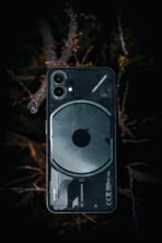 A close-up of a transparent smartphone placed on a forest floor. Modern technology meets nature's beauty.